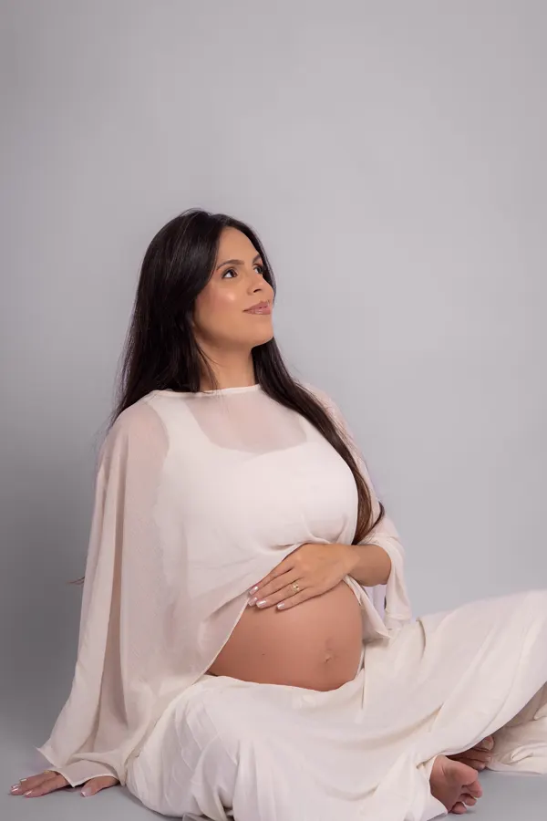 Ensaio gestante em Betim: gestante sentada com vestido branco em fundo claro