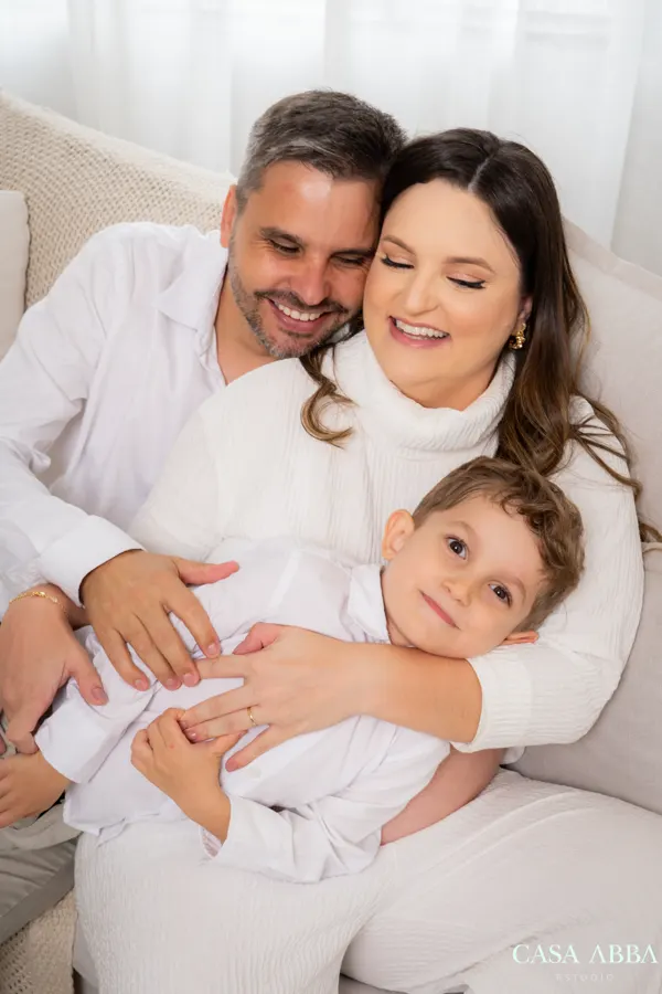 Família abraçada no sofá branco durante ensaio em Betim