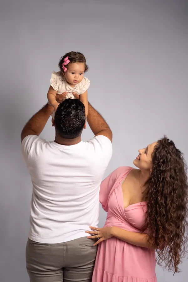 Ensaio de família em Betim: pai levantando a bebê enquanto a mãe sorri