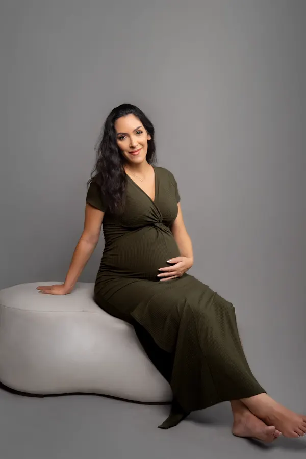 Gestante de vestido verde sentada em pufe no estúdio