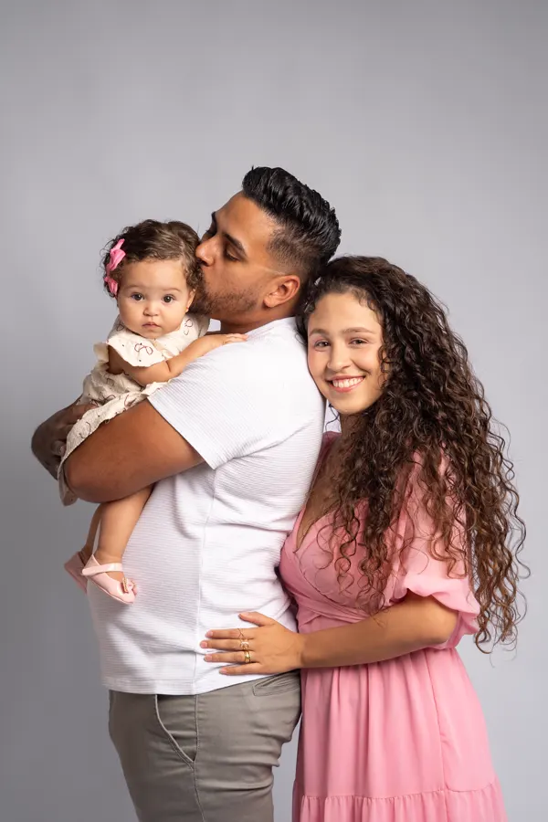 Pai beijando a bebê no colo ao lado da mãe